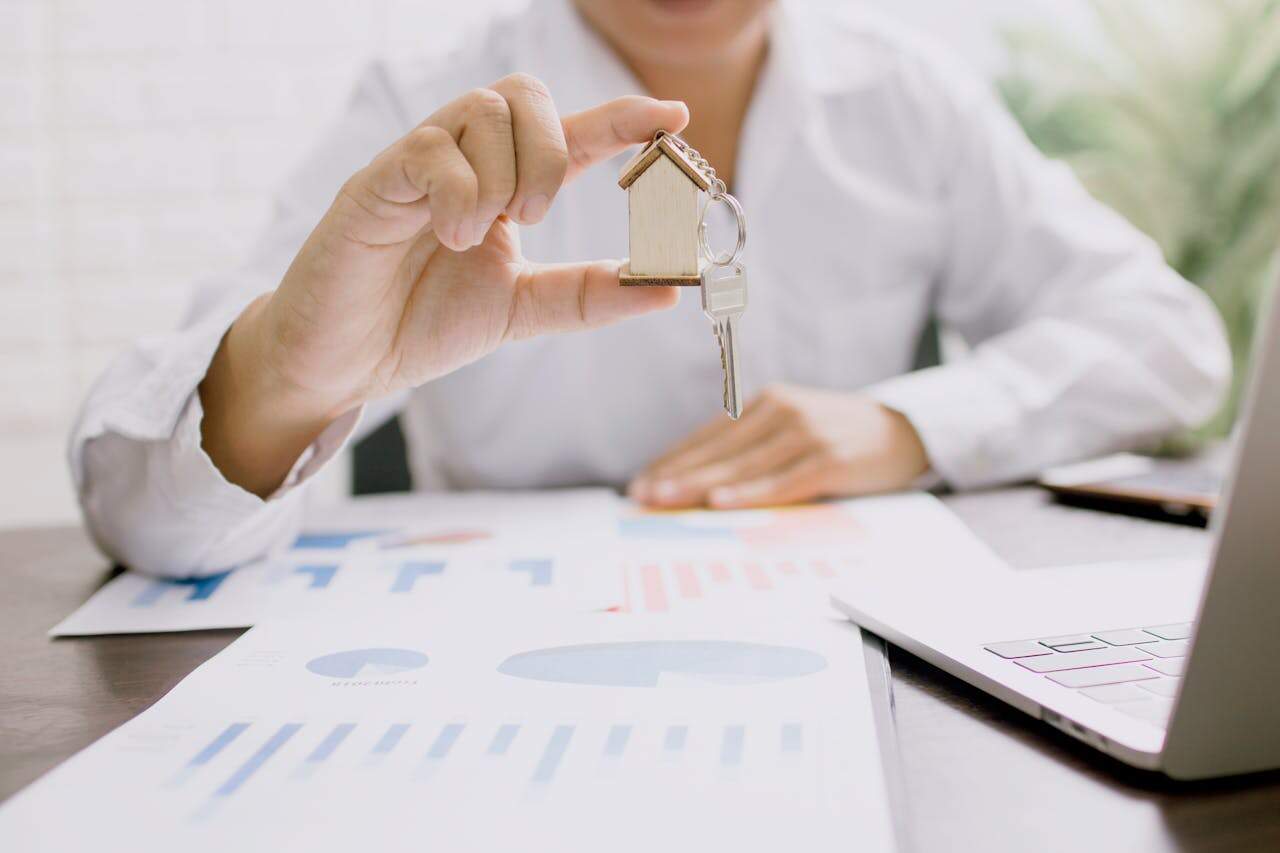 Real estate agent holding a house key with property sales documents on a desk